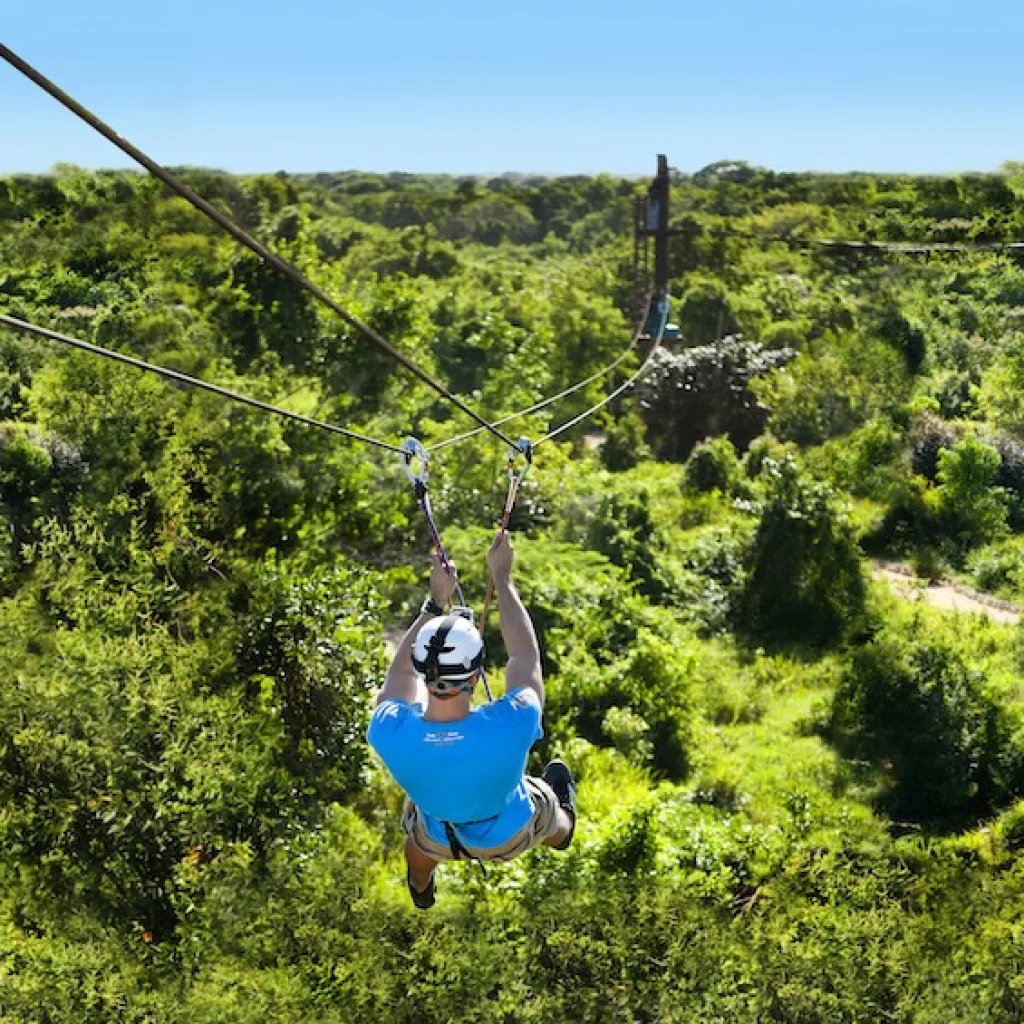 A person zip-lining over lush greenery in Bayahibe, showcasing adventure activities in a tropical setting.