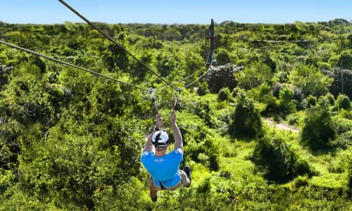 A person zip-lining over lush greenery in Bayahibe, showcasing adventure activities in a tropical setting.